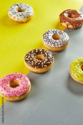 Multicolored donuts with glaze and sprinkles on a yellow-gray background