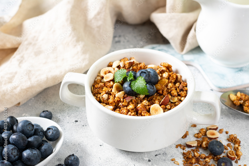 Homemade granola made from buckwheat. Organic buckwheat granola, green buckwheat sprouts, hazelnuts, pumpkin seeds, flax seeds and nutmeg. Granola in a white plate on the light gray kitchen table