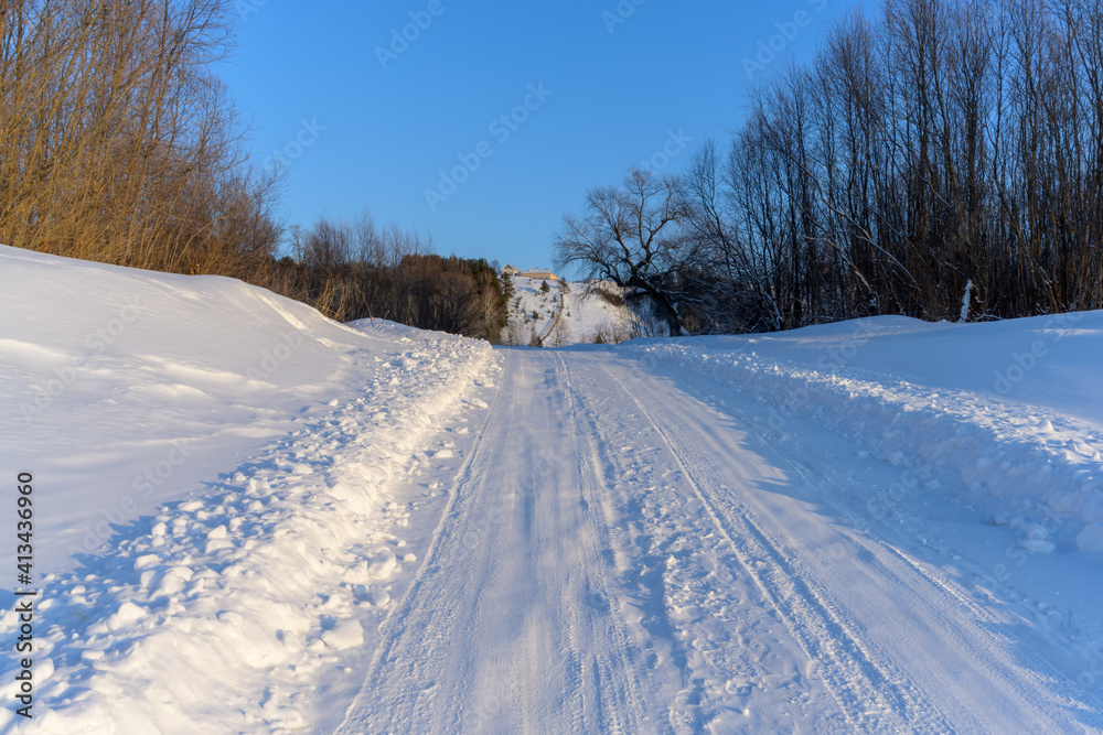 Snow covered road leading to village houses on a high mountain on a frosty winter day. various trees grow along the sides. Pure white snow and pale blue sky 