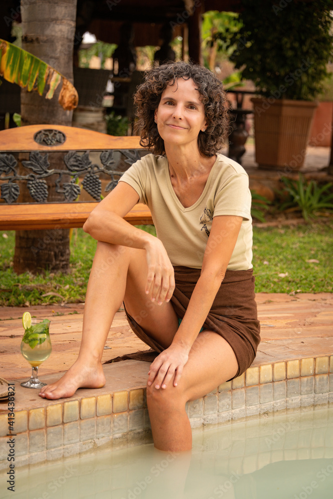 Naklejka premium Smiling brunette sitting with cocktail by pool