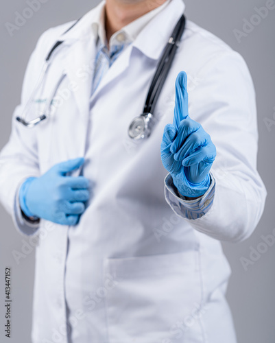 Fototapeta Naklejka Na Ścianę i Meble -  Male doctor in latex protective gloves points up with index finder on gray background. Unrecognizible medic in scrubs.