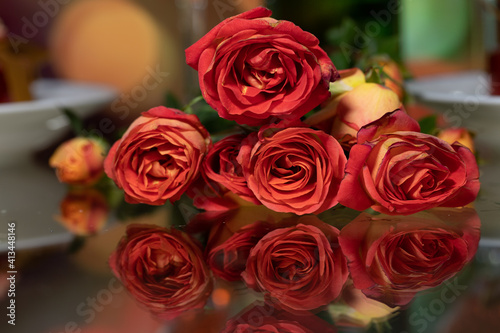 red roses with reflection on glass table setting. moving blurred colorful city night in background.