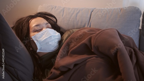 Young Asian woman suffering from coronavirus and uses mask blanket to keep warm