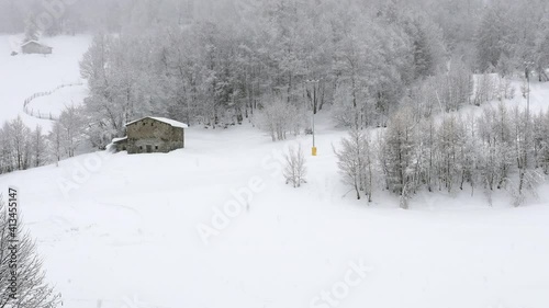 Heavy snow falling in the ski area of Aprica, in Valtellina, Italy. Area closed for Covid restrictions. Peaceful white and silence, old stone house in the distance. 