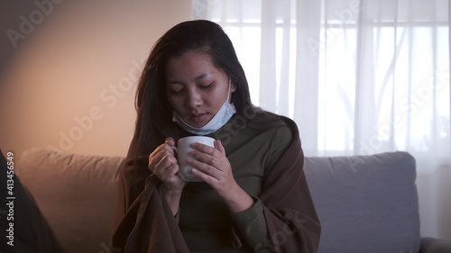 Sick Asian woman drinking lukewarm water and uses masks and blankets to warm