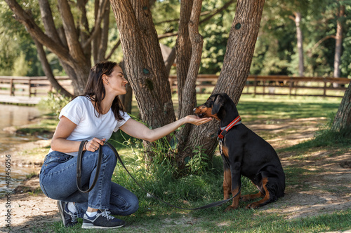 Quadro su tela Caucasian brunette woman in white t-shirt spends time with doberman soy dog outd