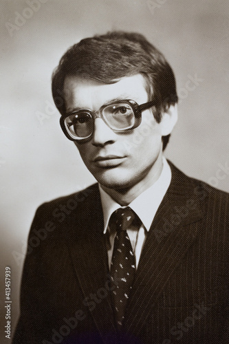 Portrait of young Soviet guy with glasses, in jacket and tie. Vintage black and white paper photo, 1970s. Transferred property, family archive. Outdated quality