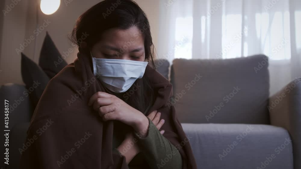 Young Asian woman drinking lukewarm water in times of suffering has chilling black eyelids all over her body due to a cold and uses masks and blankets to warm and quarantine herself Young Asian woman drinking lukewarm water in times of suffering has chilling black eyelids all over her body due to a cold and uses masks and blankets to warm and quarantine herself
