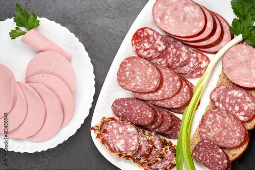 Slices of different sausages on white plates, top view.