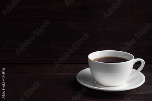 Black strong espresso coffee in a white ceramic cup. Wooden dark background, copy space.