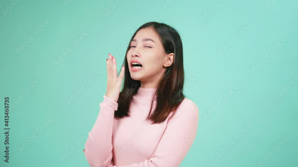 Close up portrait young Asian beautiful woman bored yawning tired covering mouth with hand. Female sleepy restless and sleepiness isolated on blue background Close up portrait young Asian beautiful woman bored yawning tired covering mouth with hand. Female sleepy restless and sleepiness isolated on blue background