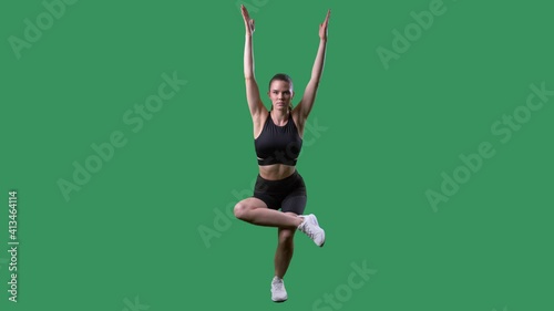 Fit woman exercises single leg squat figure four pose with outstretched arms. Full body on chroma key green screen.