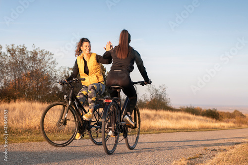 Young and happy best female friends in sportswear riding mountain bikes together in nature