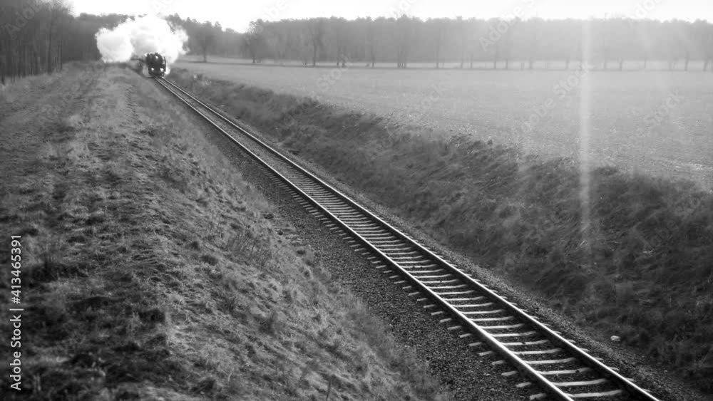 Vintage steam locomotive with old wagons on trail. Black and white footage of train with white smoke on railroad. Retro passenger transport and travel.