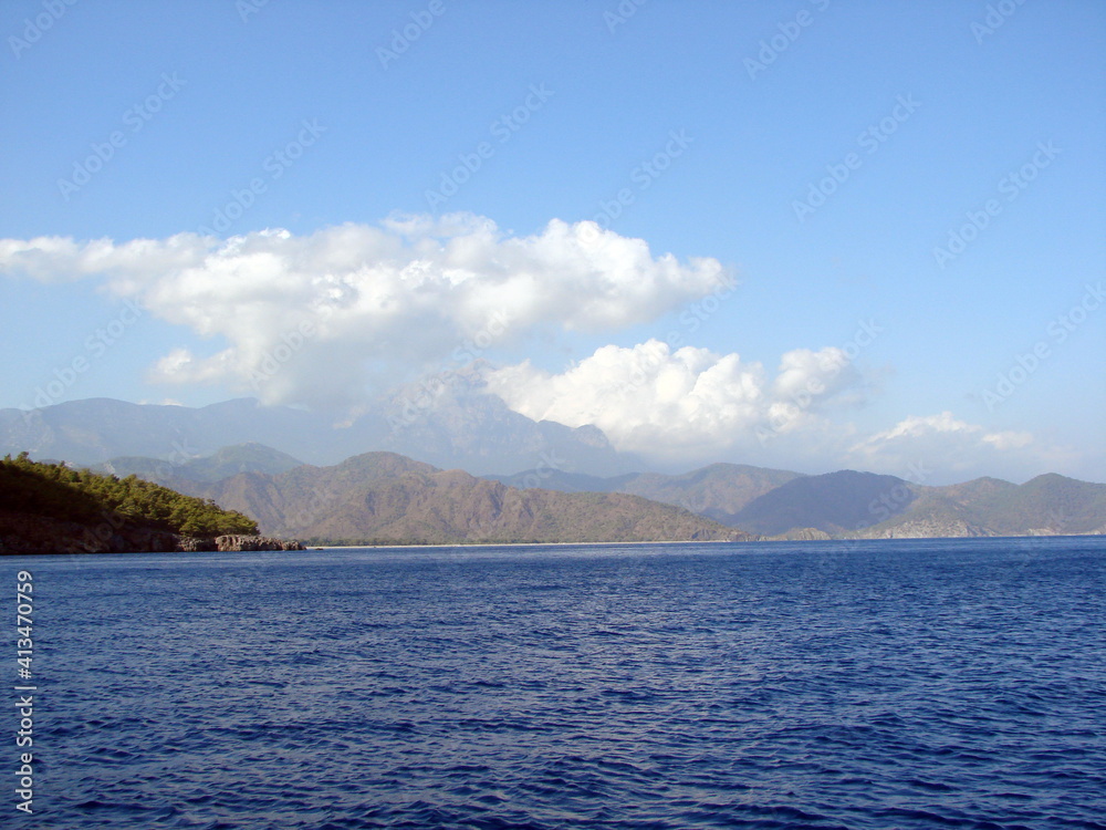 Landscape of the calm azure surface of the sea bay surrounded by rocky ridges under a cloudy evening sky at sunset. Landscape of the calm azure surface of the sea bay surrounded by rocky ridges under a cloudy evening sky at sunset.