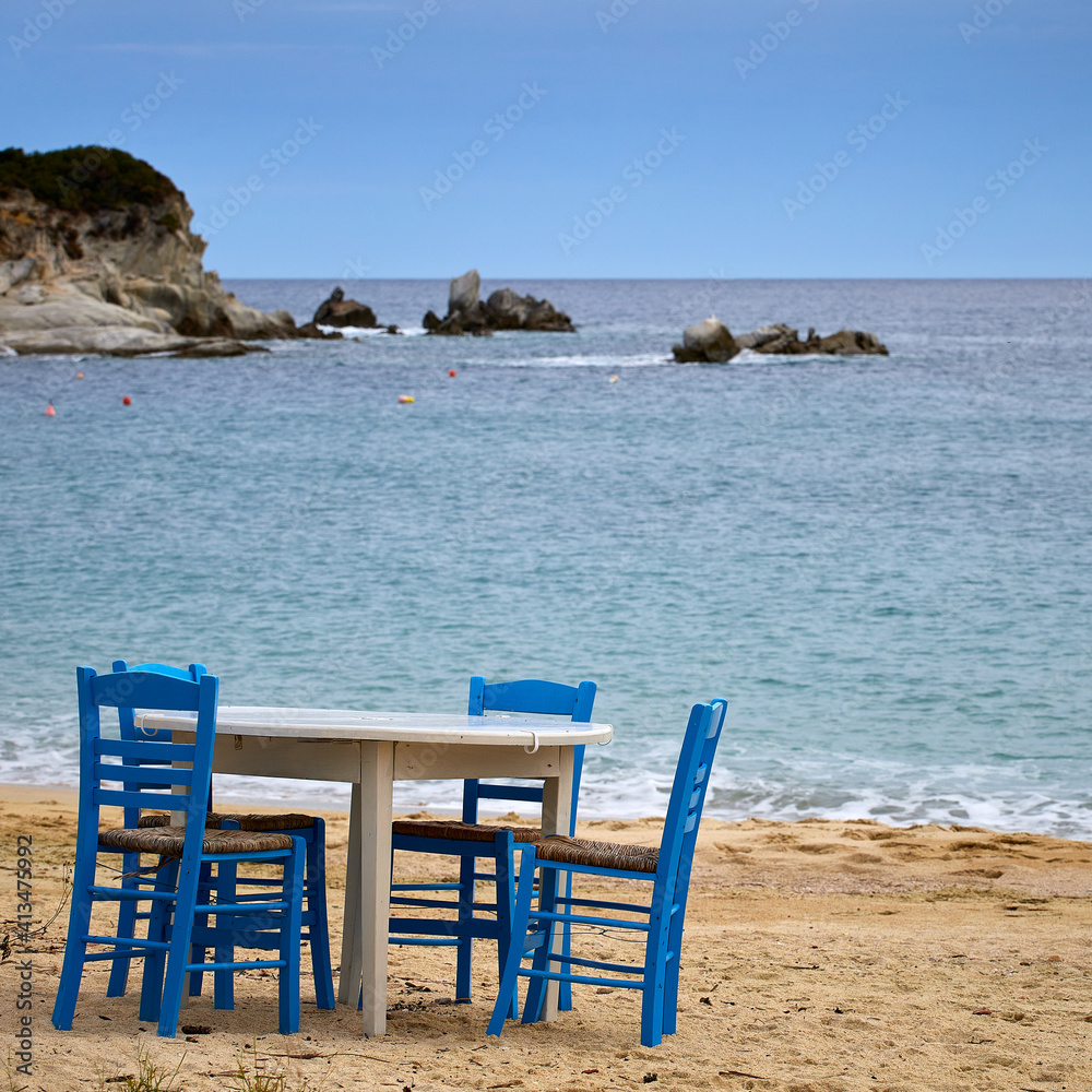 Table with traditional blue chairs at a sandy beach on Sythonia Peninsula, Greece