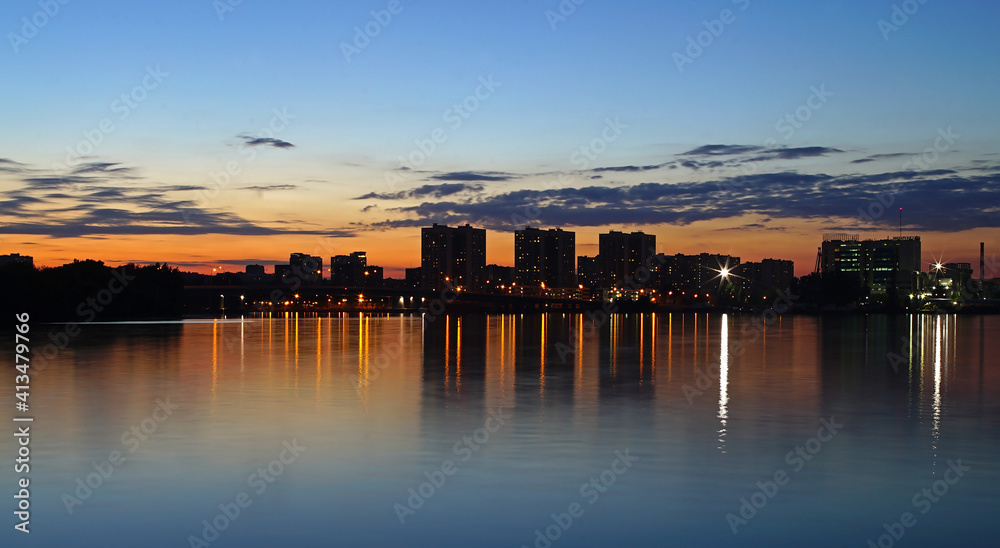 River surface in the city at sunset. Reflection of the city lights in the water. Blue sky and water.