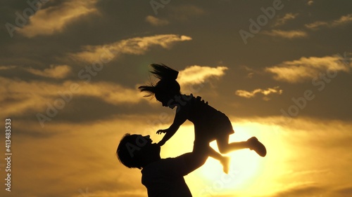 Father and little child play, laugh and hug together. Dad throws up happy daughter in blue sky. Happy family travels. Baby in arms of the parent. Dad day off. Concept of a happy family. Silhouette