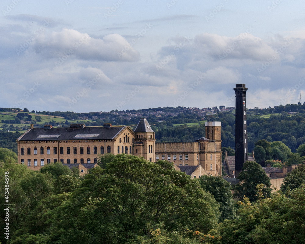 The Victorian textile mill and chimney provide a stark contrast against the green background provided by the countryside around Bingley in West Yorkshire