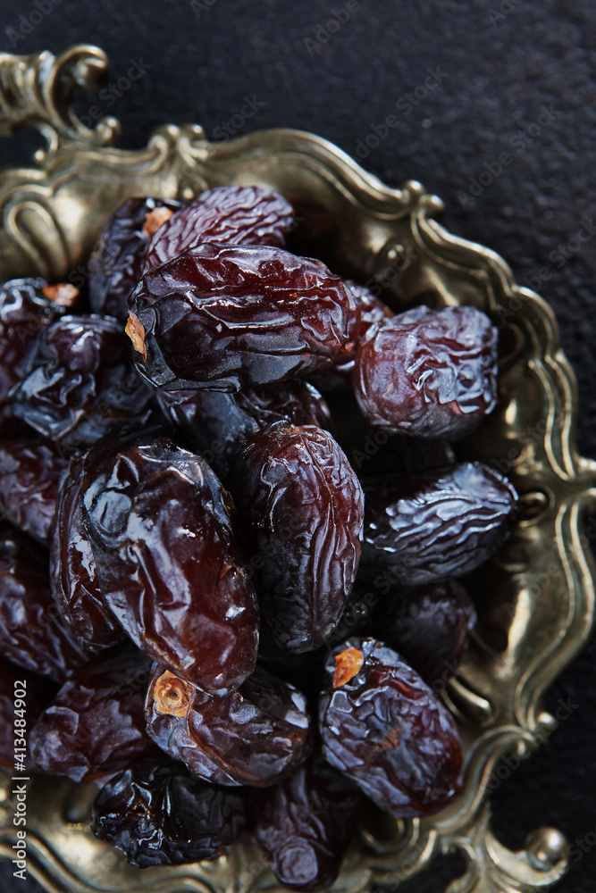 Ripe dates on an old copper platter. Juicy dried fruits. Healthy food. Fast food. Food for vegetarians. Vertical photo. Ripe dates on an old copper platter. Juicy dried fruits. Healthy food. Fast food. Food for vegetarians. Vertical photo.