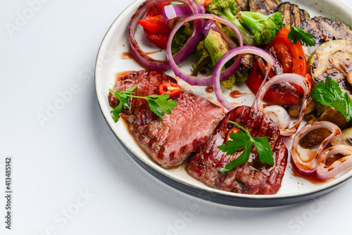 Grilled beefsteak and baked vegetables salad on a white plate over white background. Italian cuisine concept.