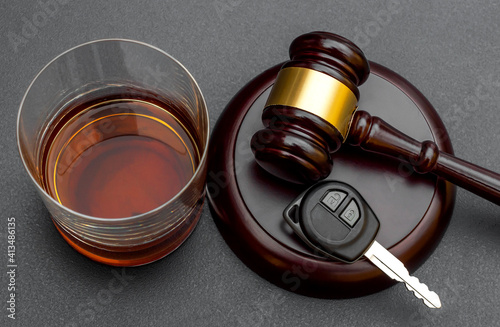 Judge's gavel with car key and glass of whiskey on black.