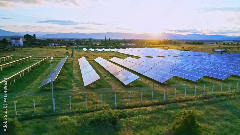 Aerial lateral motion view on solar power plant, beautiful nature with green grass field, mountains range, clean energy panels and golden sunlight sunset horizon sky Aerial lateral motion view on solar power plant, beautiful nature with green grass field, mountains range, clean energy panels and golden sunlight sunset horizon sky