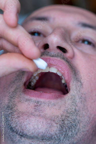 Extreme closeup man face taking white pill, mouth view swallowing pills, illness. man take medicine,open mouth and bring medicine to mouth. toned. vertical photo