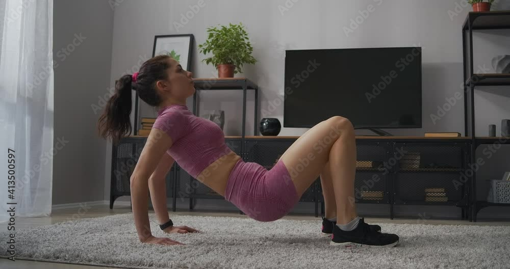 young sexy woman dressed pink sporty top and shorts is training in living room, home fitness and wellness, moving hips up young sexy woman dressed pink sporty top and shorts is training in living room, home fitness and wellness, moving hips up
