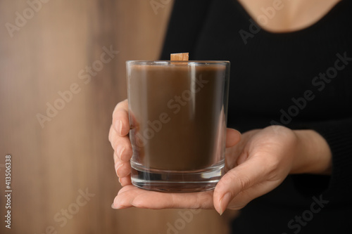Woman holding candle with wooden wick on brown background, closeup