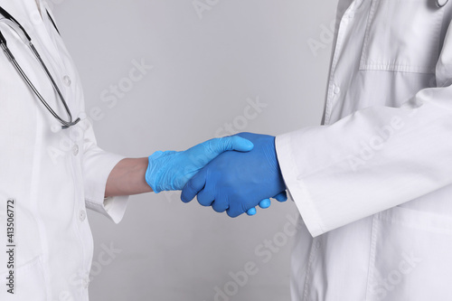 Doctors shaking hands on light grey background, closeup