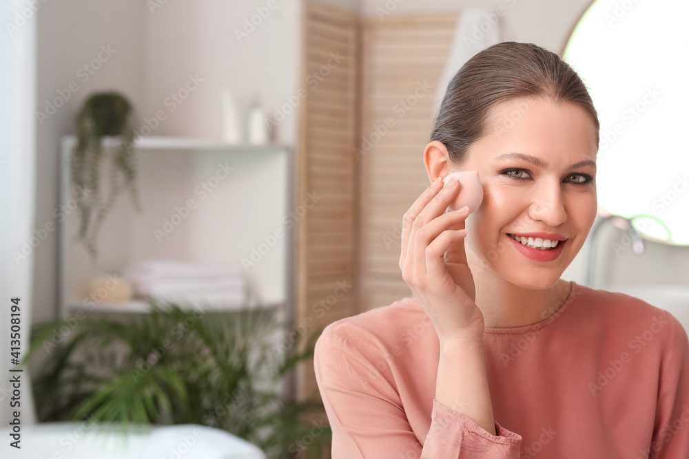 Beautiful young woman with sponge applying makeup at home Beautiful young woman with sponge applying makeup at home