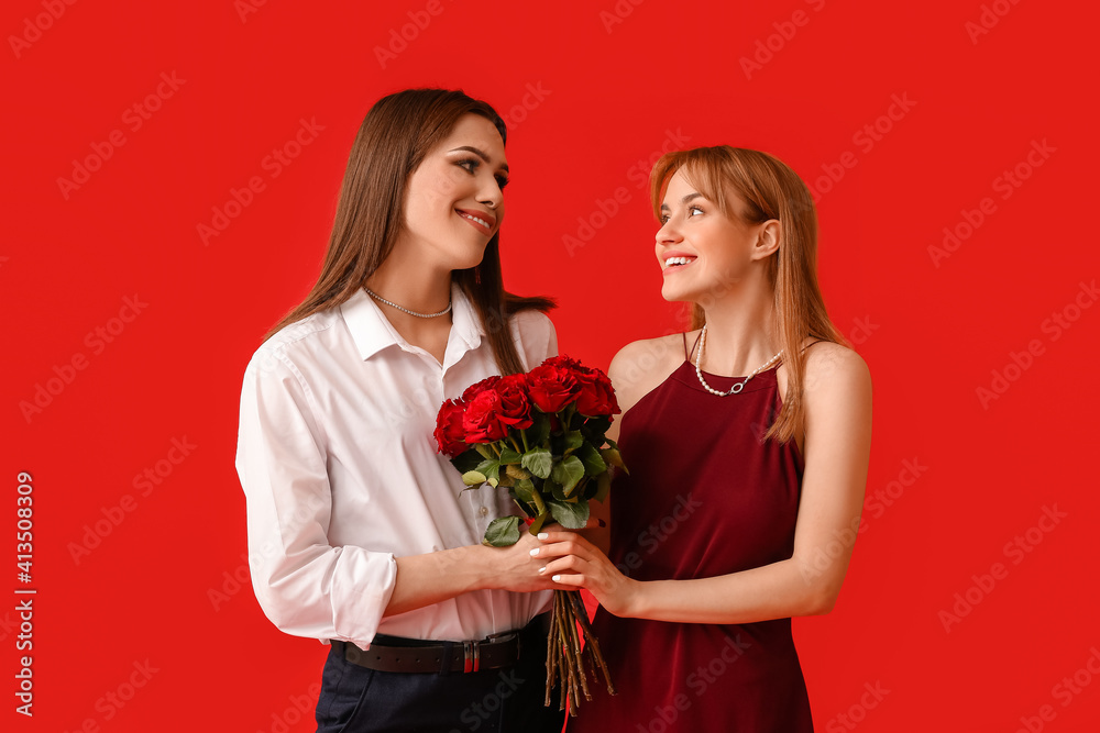 Young transgender couple with flowers on color background. Valentine's Day celebration