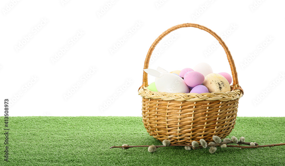 Basket with Easter eggs on grass against white background