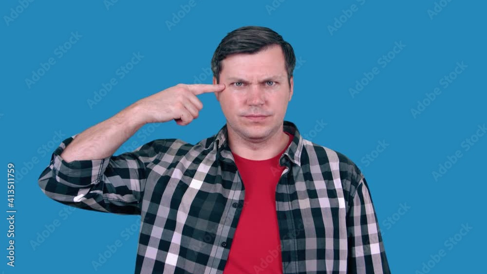 A man gesturing with a finger to his temple, wearing a plaid shirt. A man gesturing with a finger to his temple, wearing a plaid shirt.