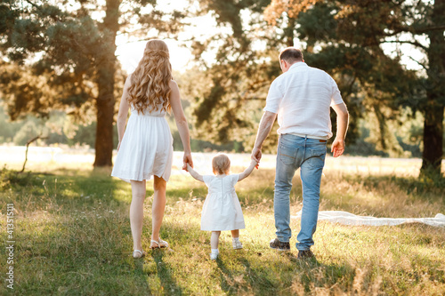 Back view of mother, father hold hands daughter enjoy nature and walk in the summer park. Young family spending time together on vacation, outdoors. Mother's, father's, baby's day © Andriy Medvediuk