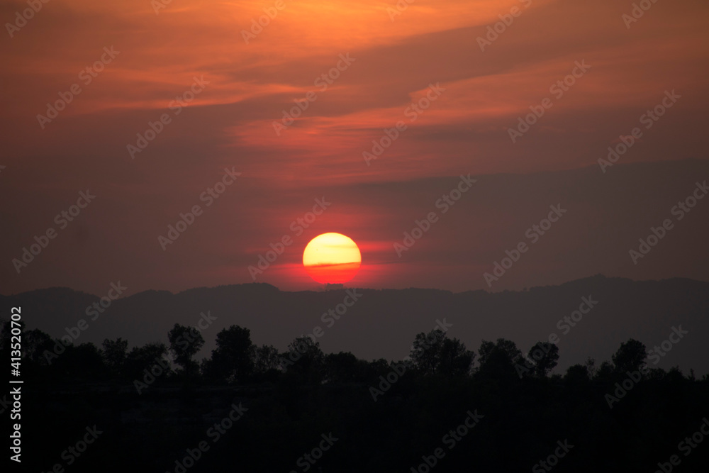 Typical sunset african lanscape with trees. Tree silhouette against a big orange round setting sun. Dark tree on open field dramatic sunrise. Sky at dawn with clouds, twilight background.