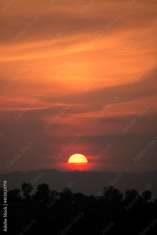 Obraz premium Typical sunset african lanscape with trees. Tree silhouette against a big orange round setting sun. Dark tree on open field dramatic sunrise. Sky at dawn with clouds, twilight background.
