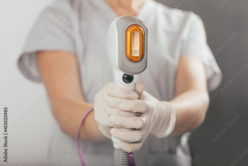 A woman tunes a laser hair removal machine. She holds a working part of the epilator A woman tunes a laser hair removal machine. She holds a working part of the epilator