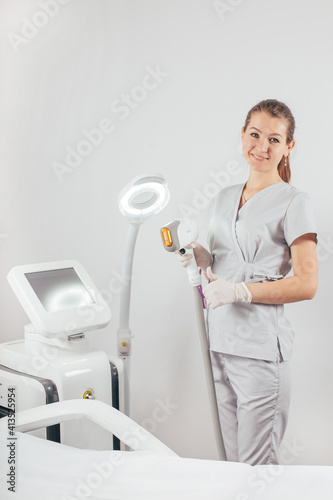 A woman tunes a laser hair removal machine. She holds a working part of the epilator in her hands and poses for a photo. It is located in a modern beauty salon. Body Care. Underarm Laser Hair Removal.