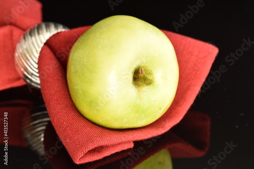 One natural green apple by Renet Simirenko with a red linen napkin, close-up, isolated on black. photo