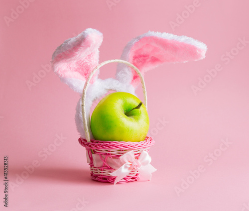 happy easter creative minimalism .wicker basket  bunny ears  headband and green apple on pink background