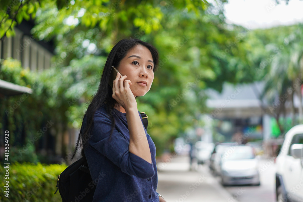 Portrait of a cheerful Asian woman waiting for taxi while using smartphone Portrait of a cheerful Asian woman waiting for taxi while using smartphone