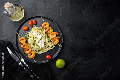 Spaghetti with green pesto and shrimps skewers, on plate, on black background, top view flat lay , with copyspace and space for text