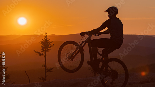Silhouette of a cyclist doing a wheelie against sunset. 