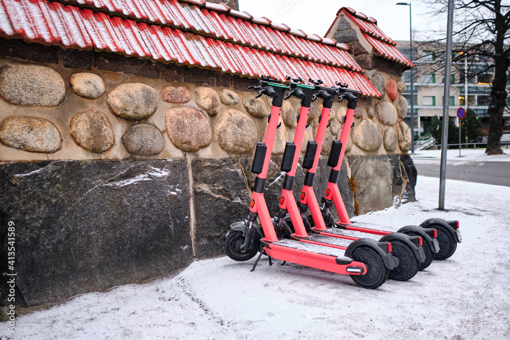 The rental electric scooters near the old stone fence in winter in the European city.