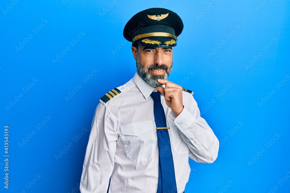 Middle age man with beard and grey hair wearing airplane pilot uniform looking confident at the camera with smile with crossed arms and hand raised on chin. thinking positive. Middle age man with beard and grey hair wearing airplane pilot uniform looking confident at the camera with smile with crossed arms and hand raised on chin. thinking positive.