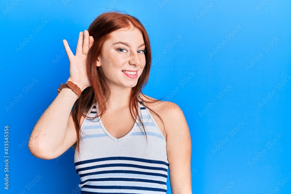 Young red head girl wearing casual clothes smiling with hand over ear listening and hearing to rumor or gossip. deafness concept. Young red head girl wearing casual clothes smiling with hand over ear listening and hearing to rumor or gossip. deafness concept.