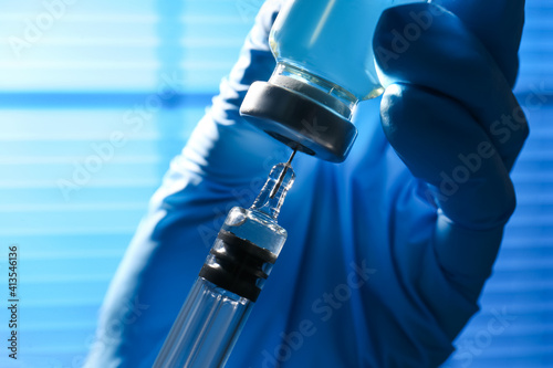 Woman filling syringe with vaccine from vial on blurred background, closeup photo