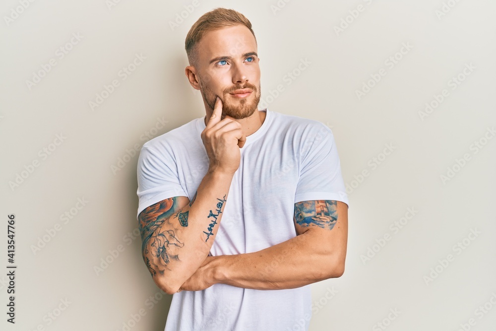 Young caucasian man wearing casual white tshirt thinking concentrated about doubt with finger on chin and looking up wondering